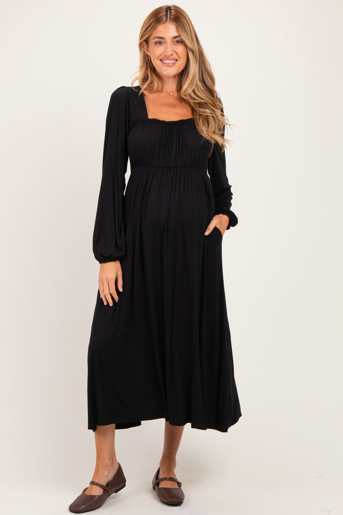 woman wearing a black long sleeve maternity dress with a smocked bodice and pockets, showcasing her baby bump