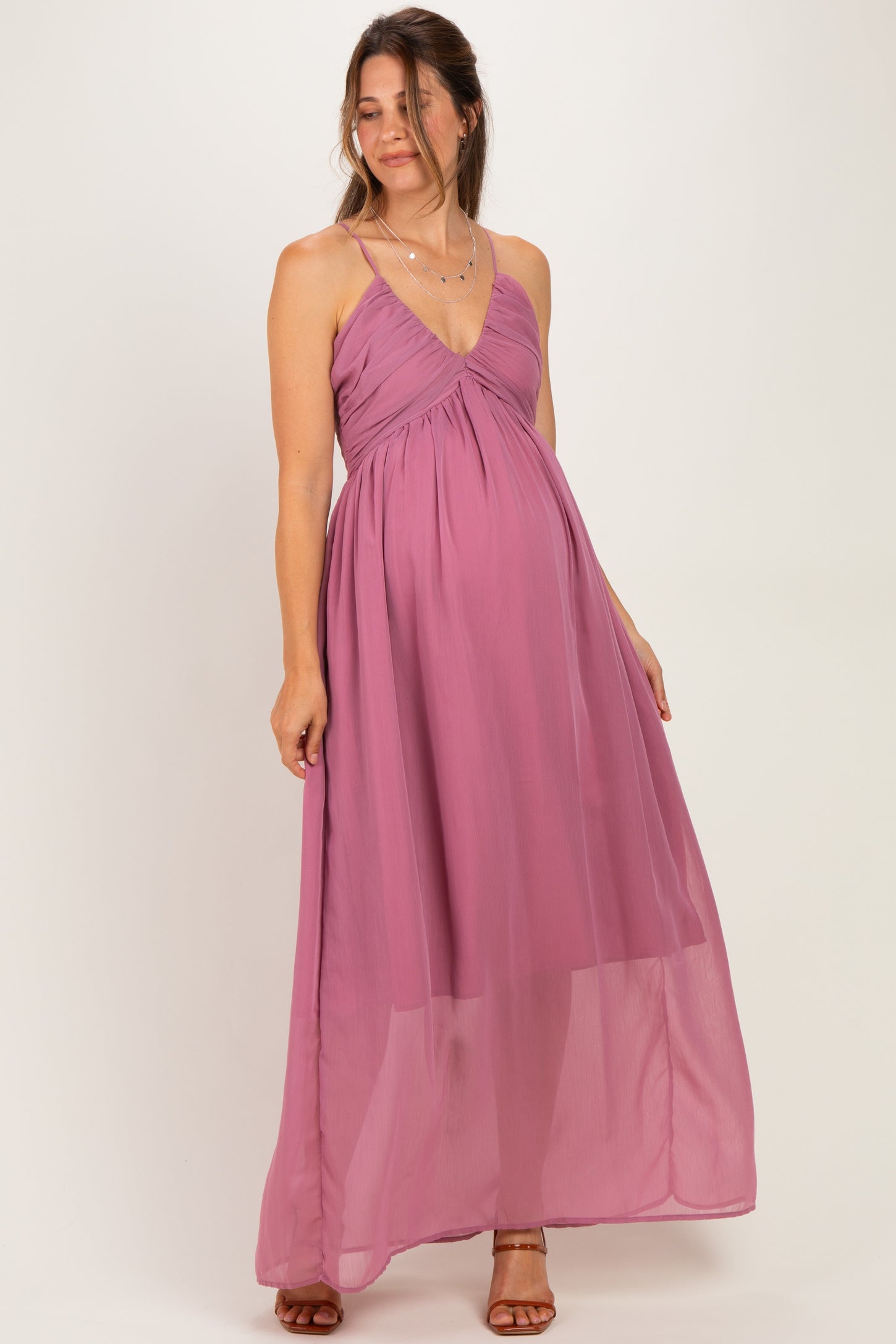 woman wearing a flowing mauve maternity dress with a v-neck and spaghetti straps, featuring a gathered bust and a baby bump visible