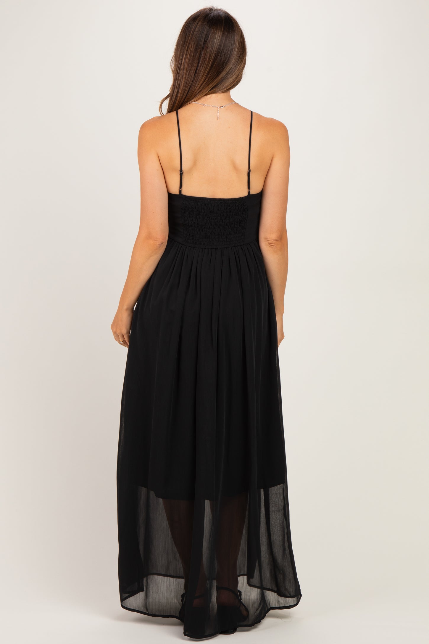 woman wearing a black maternity maxi dress with a smocked bodice and sheer overlay, showing the back view