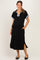 woman wearing a black maternity polo dress with blue collar details and side slits, smiling and posing with hands in pockets