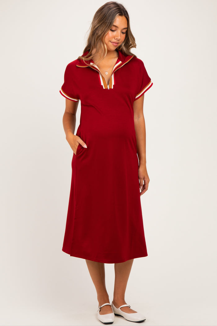 woman wearing a red maternity dress with a collar and short sleeves, featuring a sporty design and side pockets, with a visible baby bump