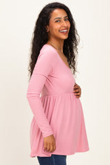woman wearing a light pink long sleeve maternity top with a babydoll style, highlighting her baby bump