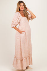 woman wearing a light pink floral maternity maxi dress with puff sleeves and a ruffled hem, showing her baby bump