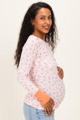 woman wearing a light pink floral long sleeve maternity top and holding her baby bump