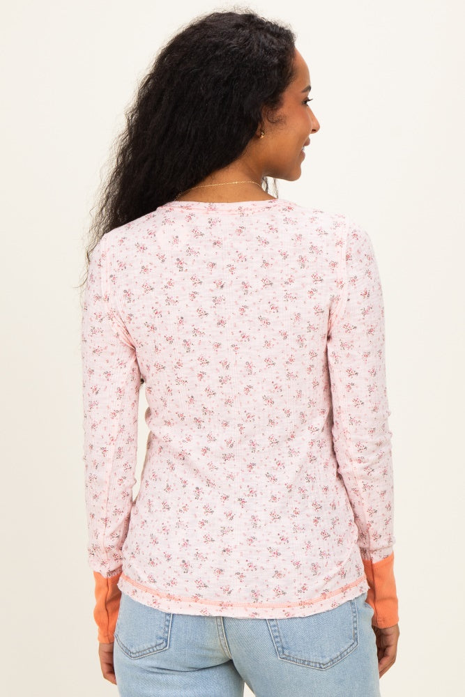 woman wearing a floral long sleeve maternity top in pink with orange cuffs, showing a side view from the back