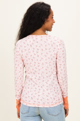 woman wearing a floral long sleeve maternity top in pink with orange cuffs, showing a side view from the back