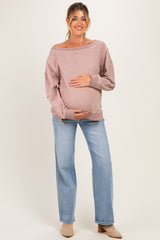woman wearing a light pink maternity sweater and blue jeans, gently cradling her baby bump