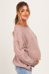 woman wearing a light pink oversized maternity sweater with a visible baby bump, styled with blue jeans