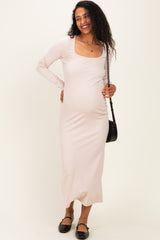 woman wearing a light pink long sleeve maternity dress, showing off her baby bump while smiling and holding a small bag