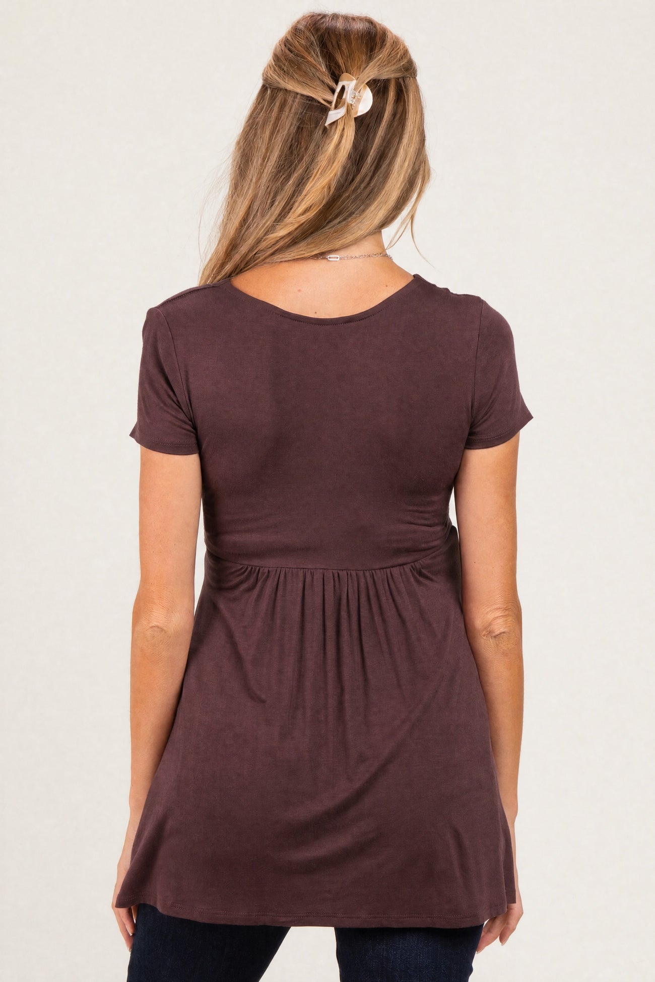 woman wearing a dark mauve short sleeve maternity top with a gathered waist and relaxed fit, seen from the back