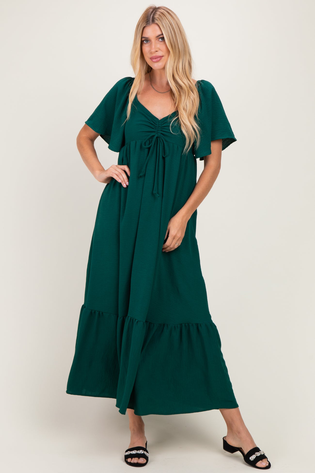 woman wearing a dark green maxi dress with flutter sleeves and a tie front detail