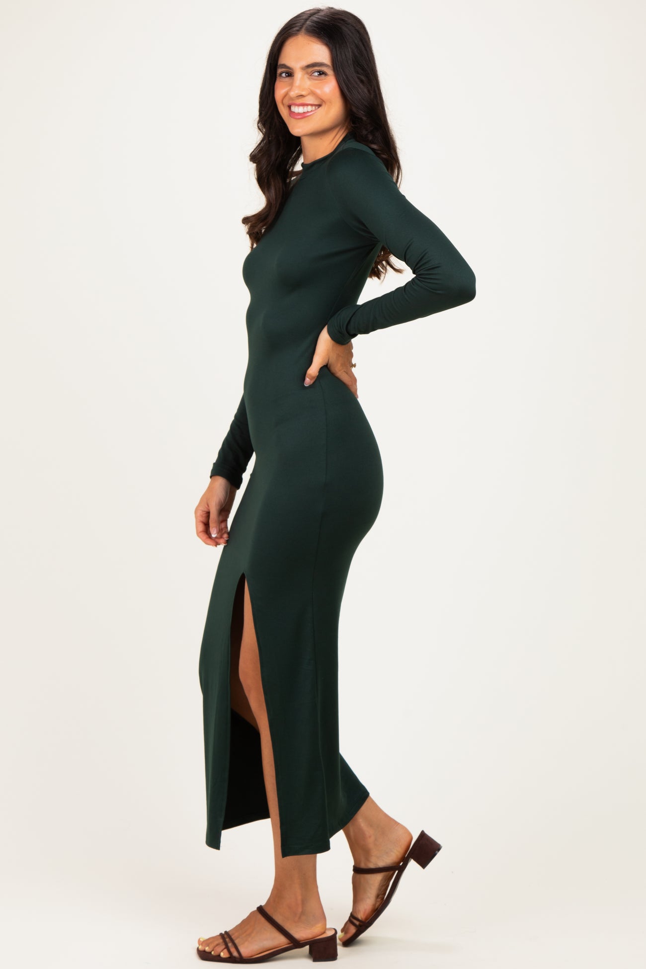 woman wearing a dark green long sleeve maxi dress with a side slit and brown sandals