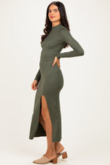 woman wearing a fitted olive green long sleeve maxi dress with a side slit and heeled mules