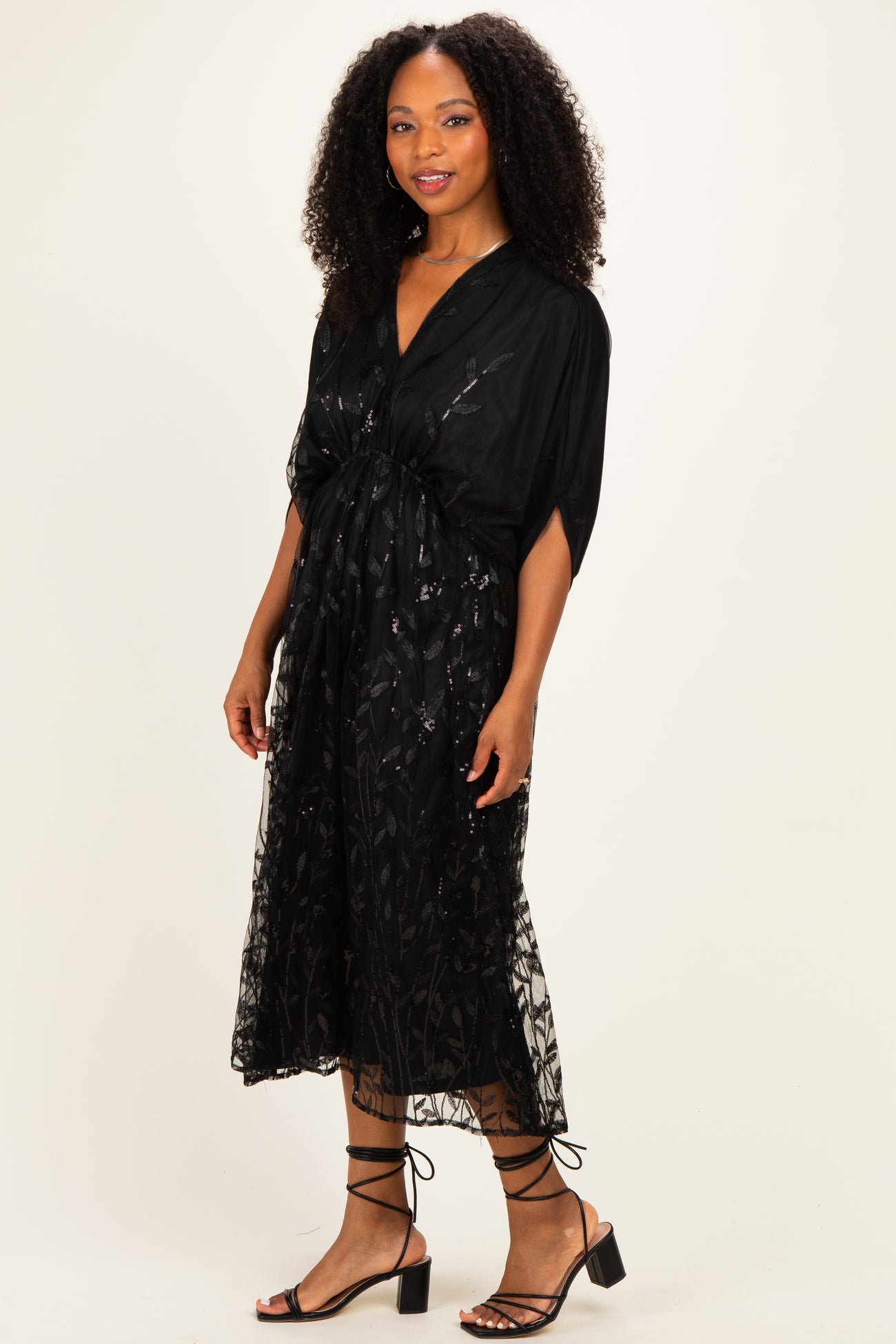 woman wearing a black floral lace midi dress with short sleeves and a fitted waist, paired with strappy black heels