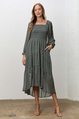 woman wearing a dark green floral mid-length dress with long sleeves and pockets, styled with strappy heels