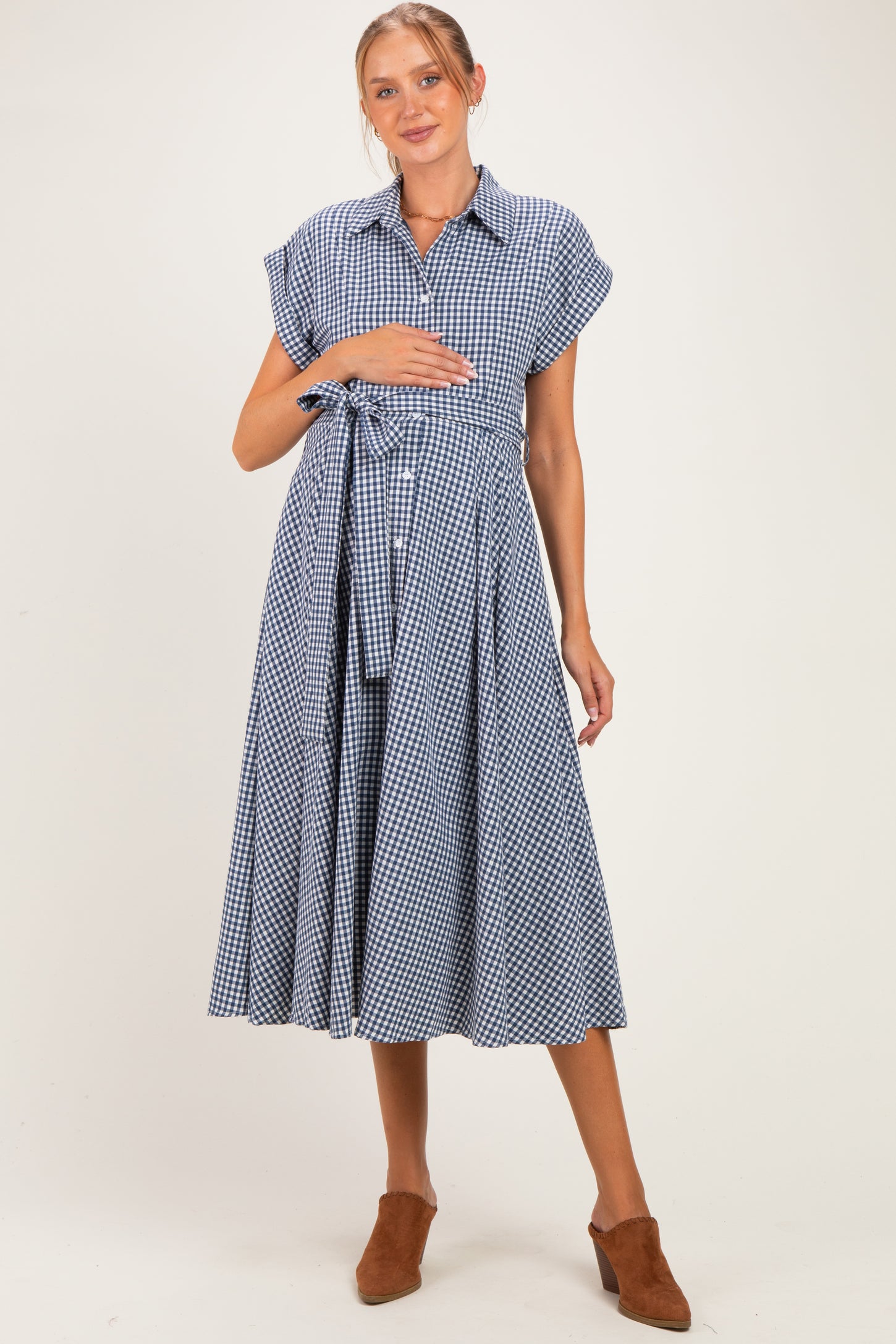 woman wearing a navy and white checkered maternity dress with short sleeves and a tie waist, holding her baby bump