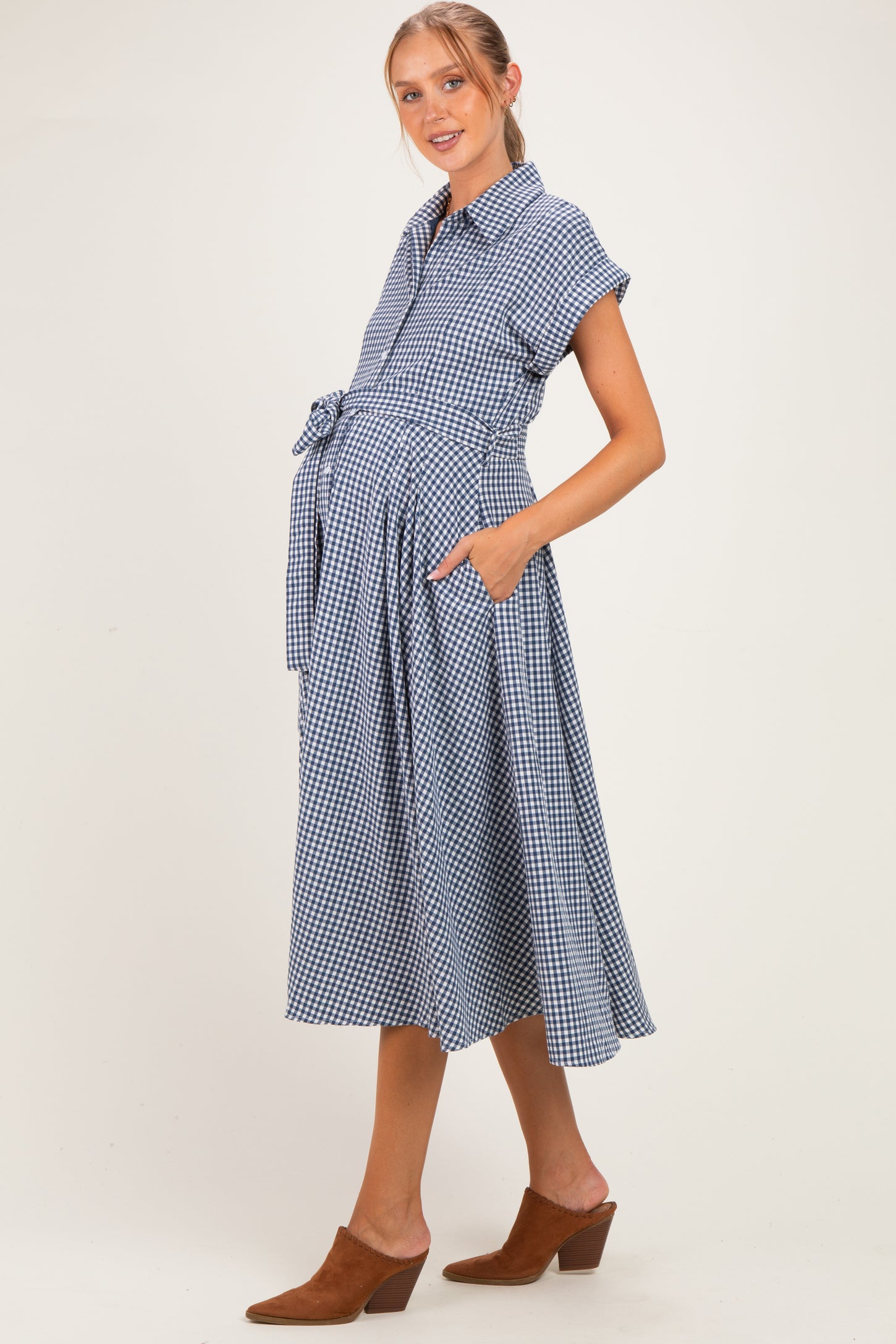 woman wearing a navy and white gingham maternity dress with short sleeves, a tie waist, and side pockets