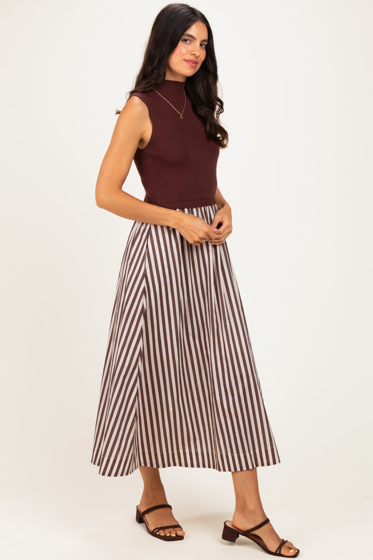 woman wearing a burgundy sleeveless top and a long brown and white striped maxi skirt with strappy sandals
