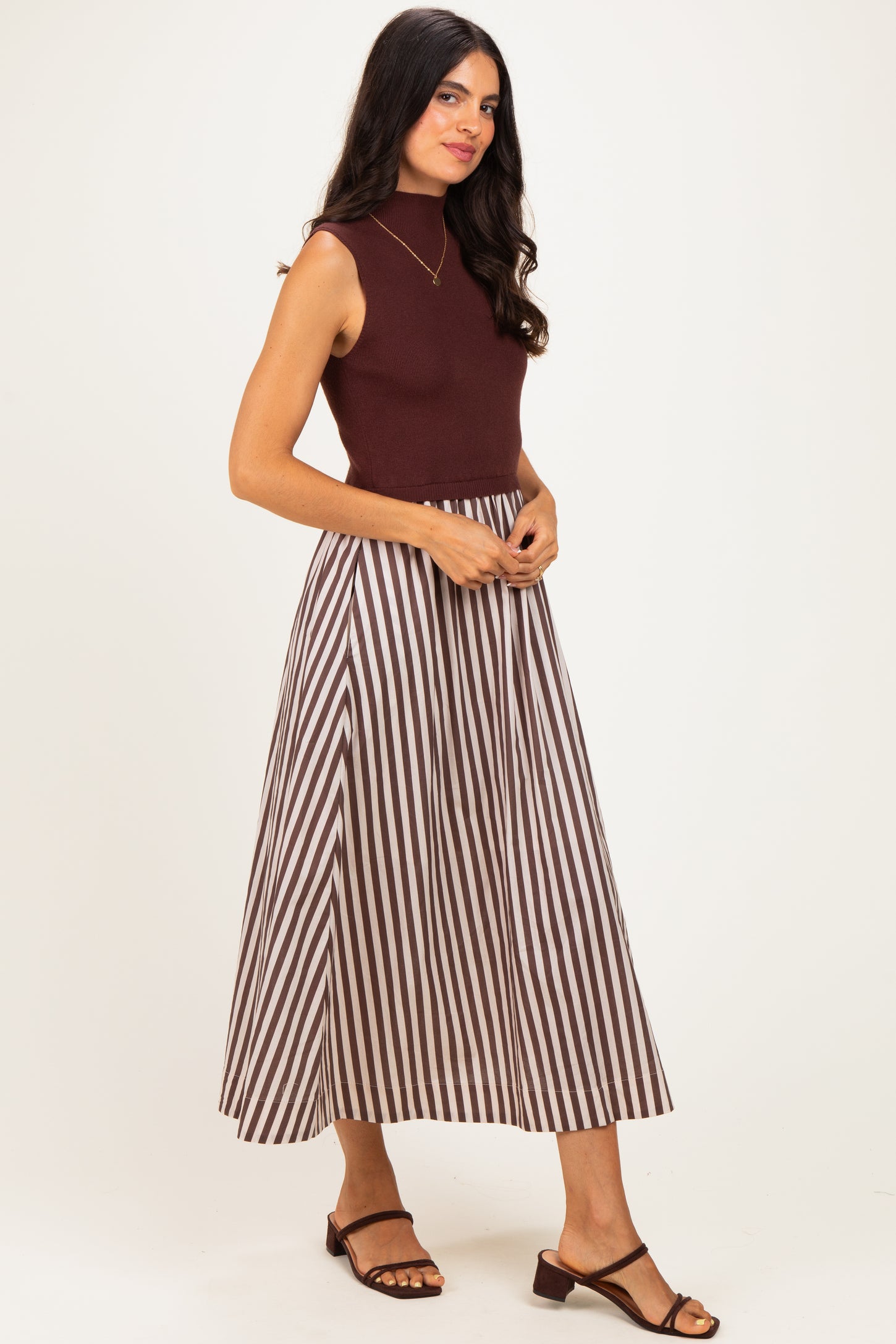 woman wearing a burgundy sleeveless top and a long brown and white striped maxi skirt with strappy sandals