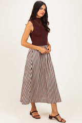 woman wearing a burgundy sleeveless top and a long brown and white striped maxi skirt with strappy sandals