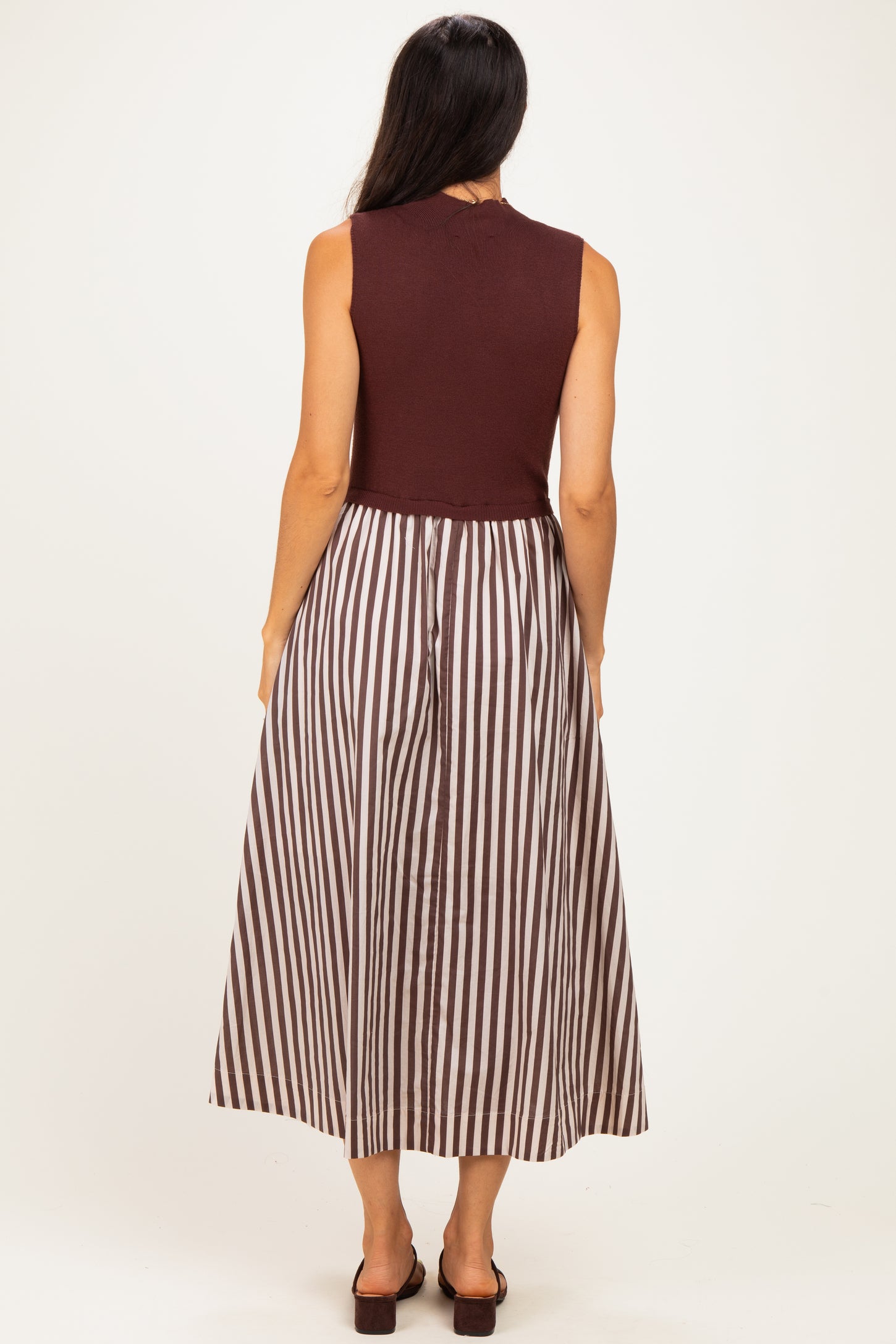 woman wearing a burgundy sleeveless top with a striped brown and white maxi skirt, seen from the back