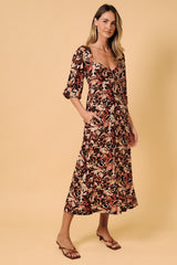 woman wearing a floral midi dress with a scooped neckline and three-quarter sleeves, standing against a beige background