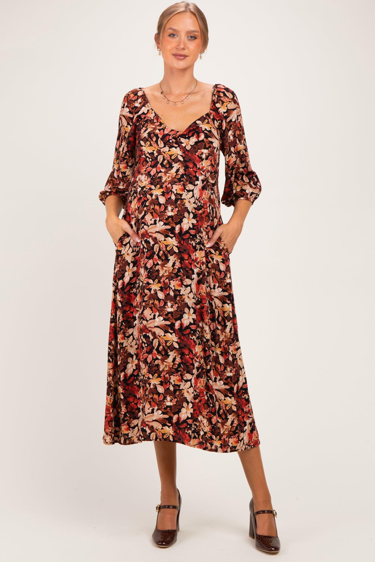 woman wearing a floral print maternity midi dress with three-quarter sleeves and pockets, showcasing her baby bump