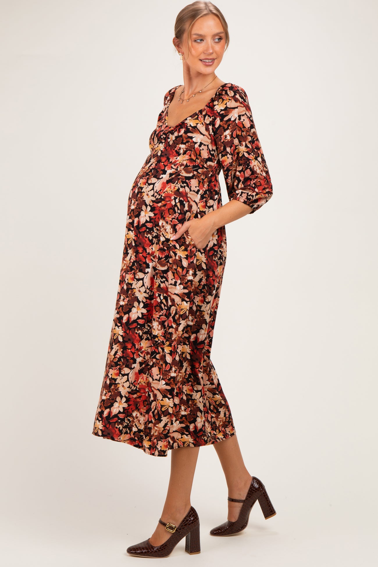 woman wearing a floral print maternity dress with pockets and three-quarter sleeves, showing her baby bump