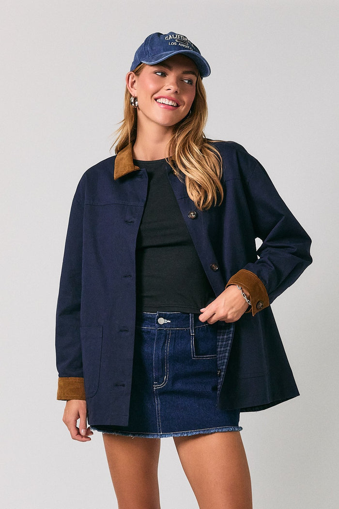 woman wearing a navy blue jacket with a brown collar, black top, denim skirt, and a blue cap