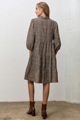 woman wearing a brown floral print tiered dress with puff sleeves and ankle boots, standing with her back to the camera