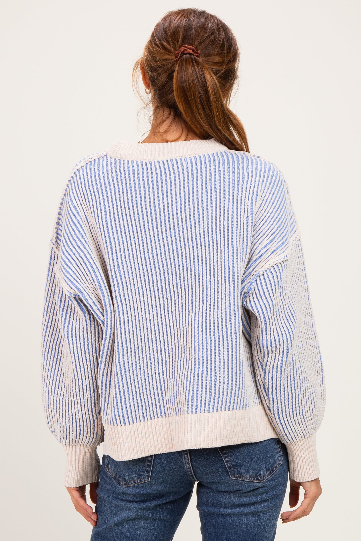 woman wearing a cream and blue striped oversized sweater paired with blue jeans, seen from the back