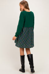 woman wearing a green cropped sweatshirt and a plaid maternity dress with a flowy skirt, showing her baby bump