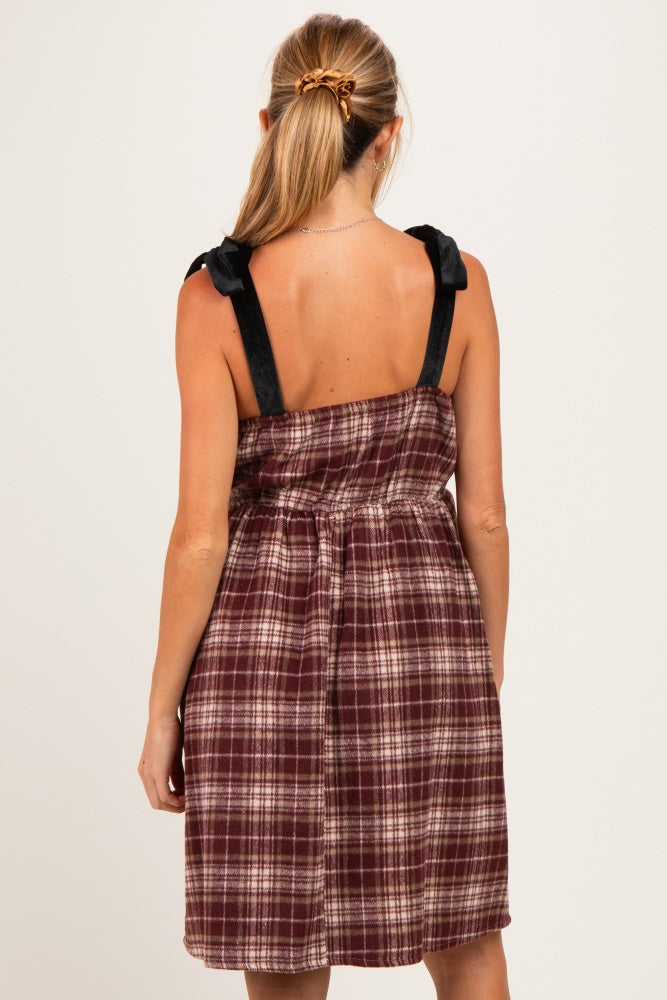 woman wearing a burgundy plaid maternity dress with black strap details, showing the back view