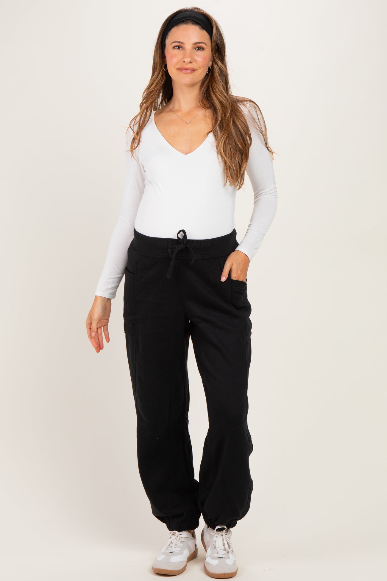 woman wearing a white long sleeve maternity bodysuit and black maternity jogger pants with pockets and drawstring waist