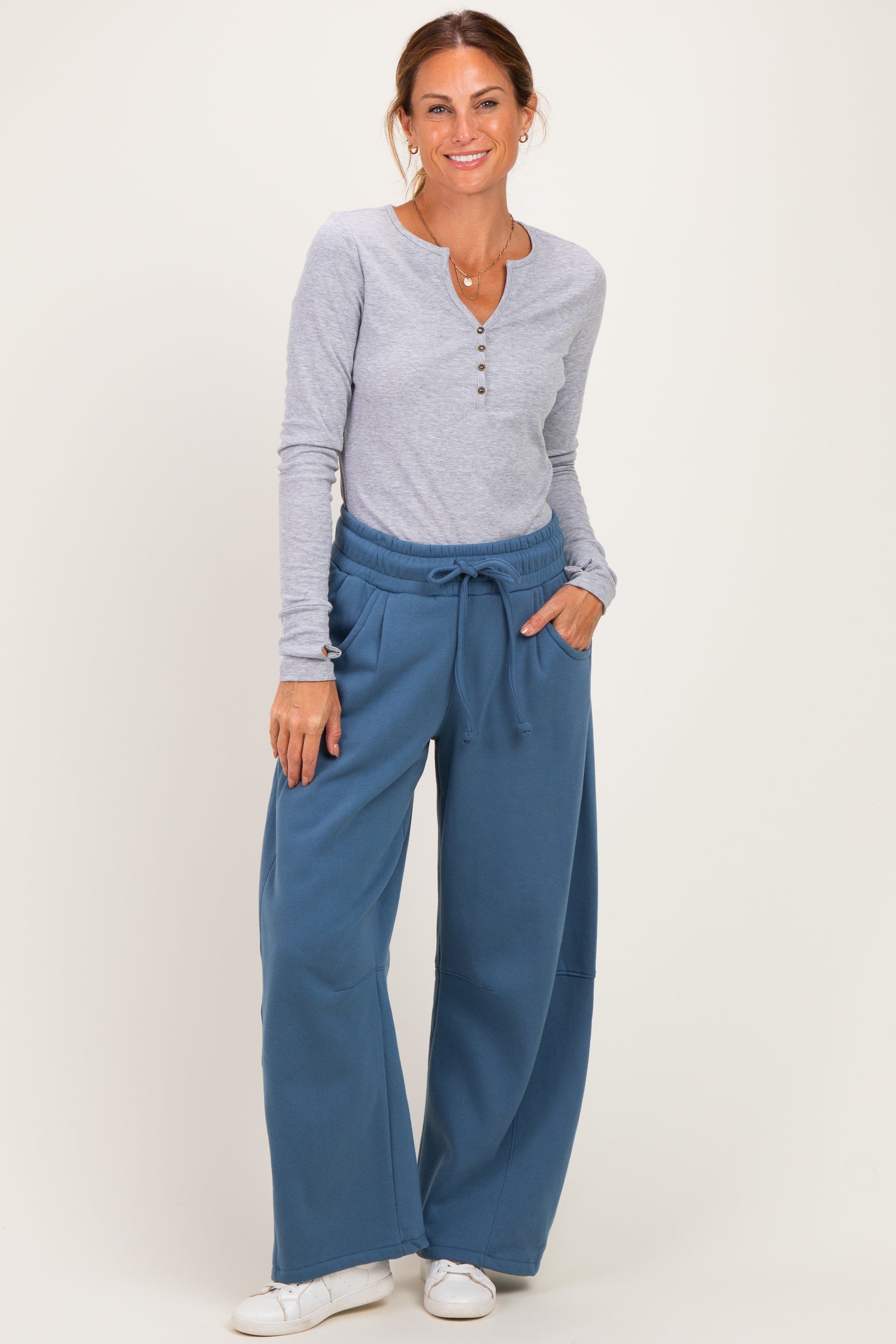 woman wearing a gray long sleeve henley top and blue wide-leg sweatpants with pockets