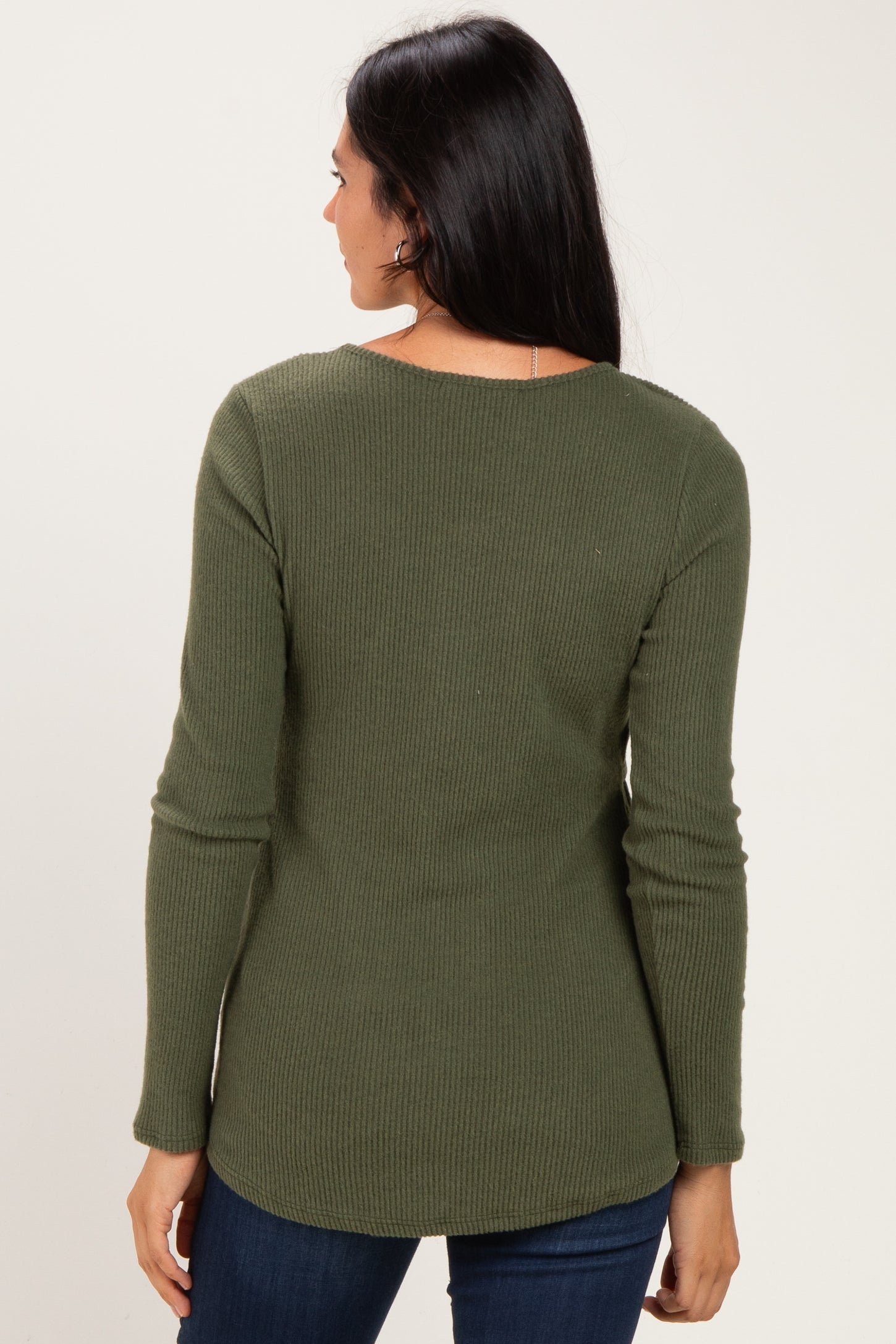 woman wearing a dark olive green ribbed long sleeve top, seen from the back with a rounded hem