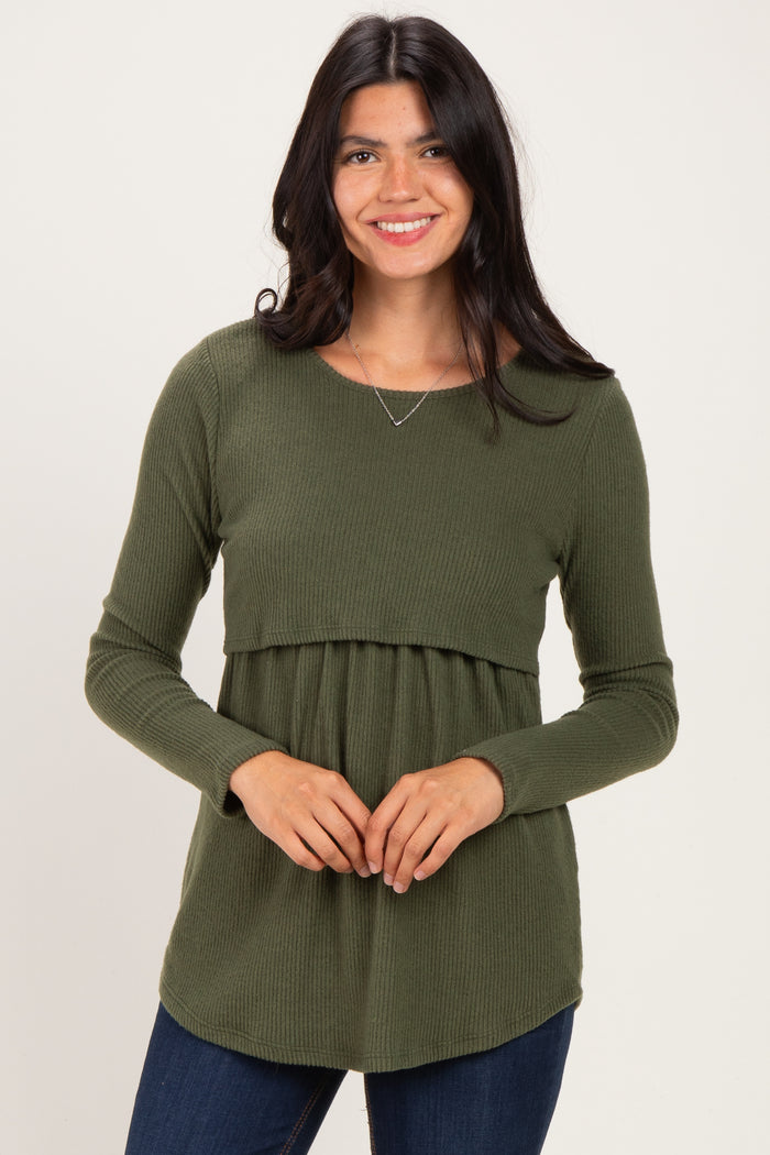 woman wearing a dark green long sleeve ribbed top with a fitted bodice and flowy bottom, smiling at the camera