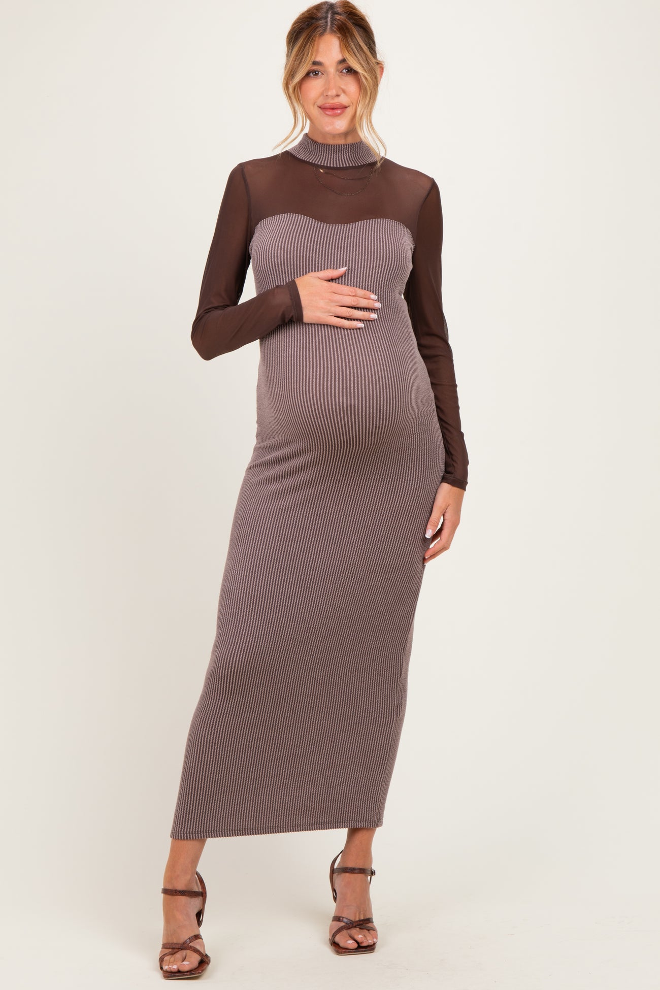 woman wearing a brown ribbed maternity dress with long sheer sleeves and a fitted silhouette, holding her baby bump