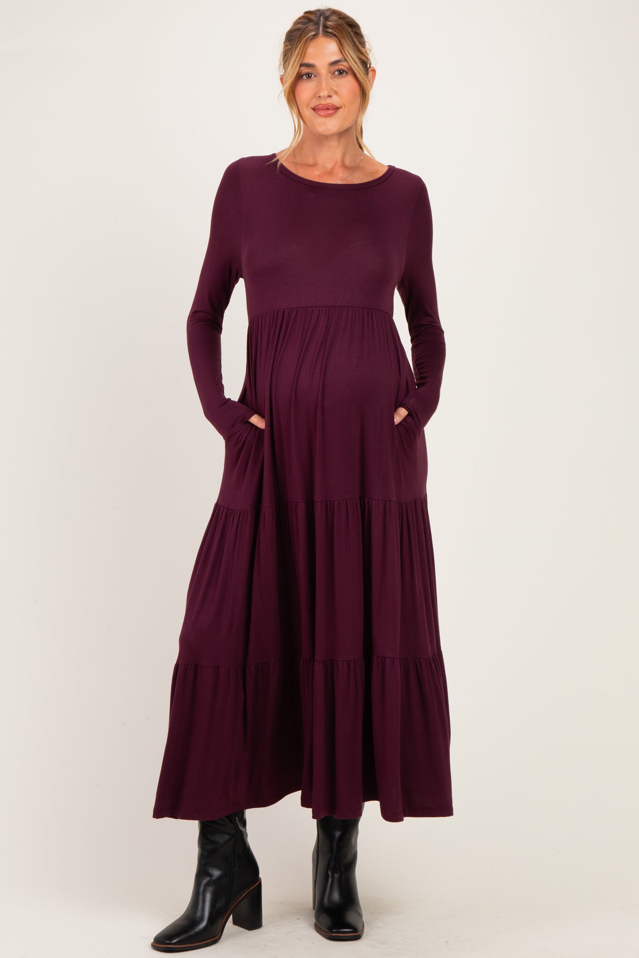 woman wearing a dark purple long sleeve maternity dress with tiered design and pockets, showcasing her baby bump