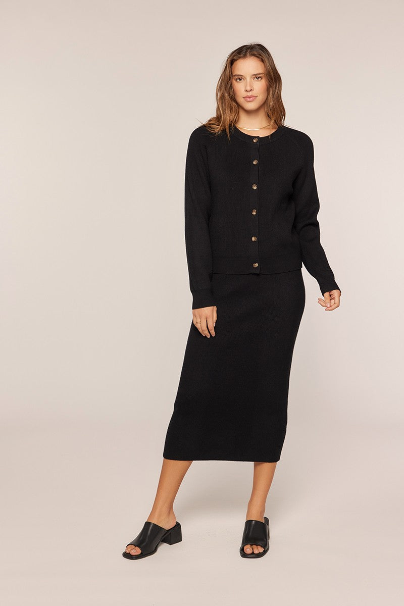 woman wearing a black cardigan and matching midi skirt with buttons and a straight silhouette
