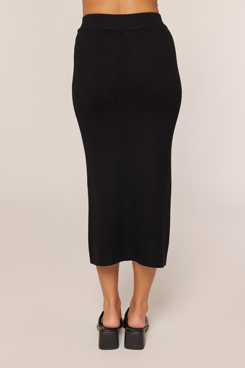 woman wearing a black ribbed midi skirt, shown from the back, with a fitted silhouette and a comfortable waistline