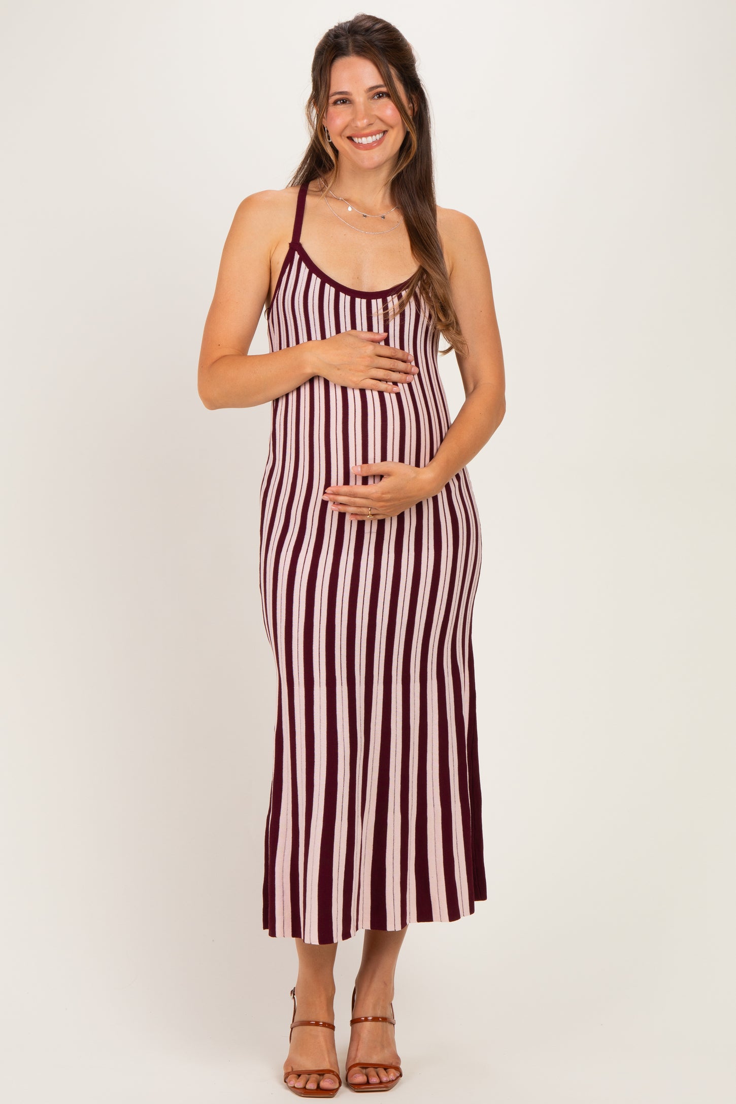 woman wearing a maroon and white striped maternity maxi dress and holding her baby bump