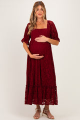 woman wearing a burgundy lace maternity dress with short puff sleeves and a tiered hem, holding her baby bump