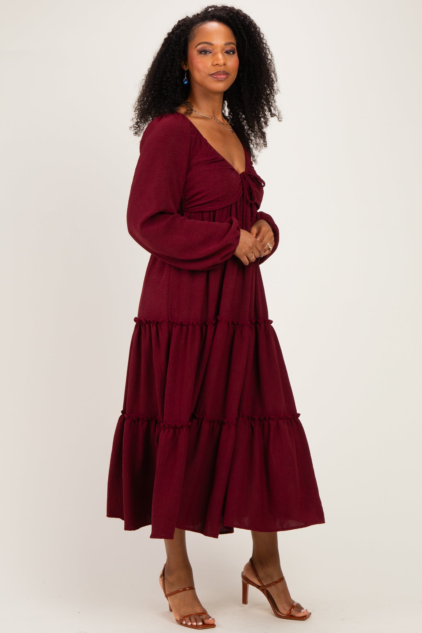 woman wearing a burgundy maxi dress with a deep v-neckline and tiered ruffle detailing, styled with heeled sandals