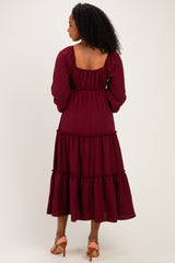 woman wearing a burgundy long sleeve tiered midi dress with a square back and ruffle details