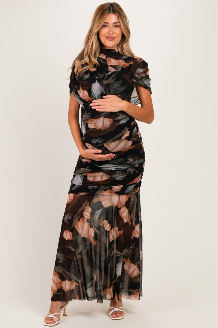 woman wearing a black floral print maternity dress with ruching and a flowing skirt, cradling her baby bump