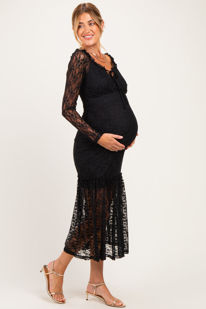 woman wearing a black lace maternity dress with long sleeves and a ruffled hem, smiling and showing her baby bump