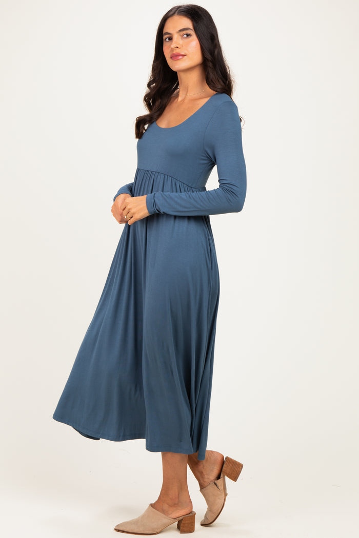woman wearing a deep blue long sleeve maxi dress with a fitted bodice and flowing skirt, paired with beige mules