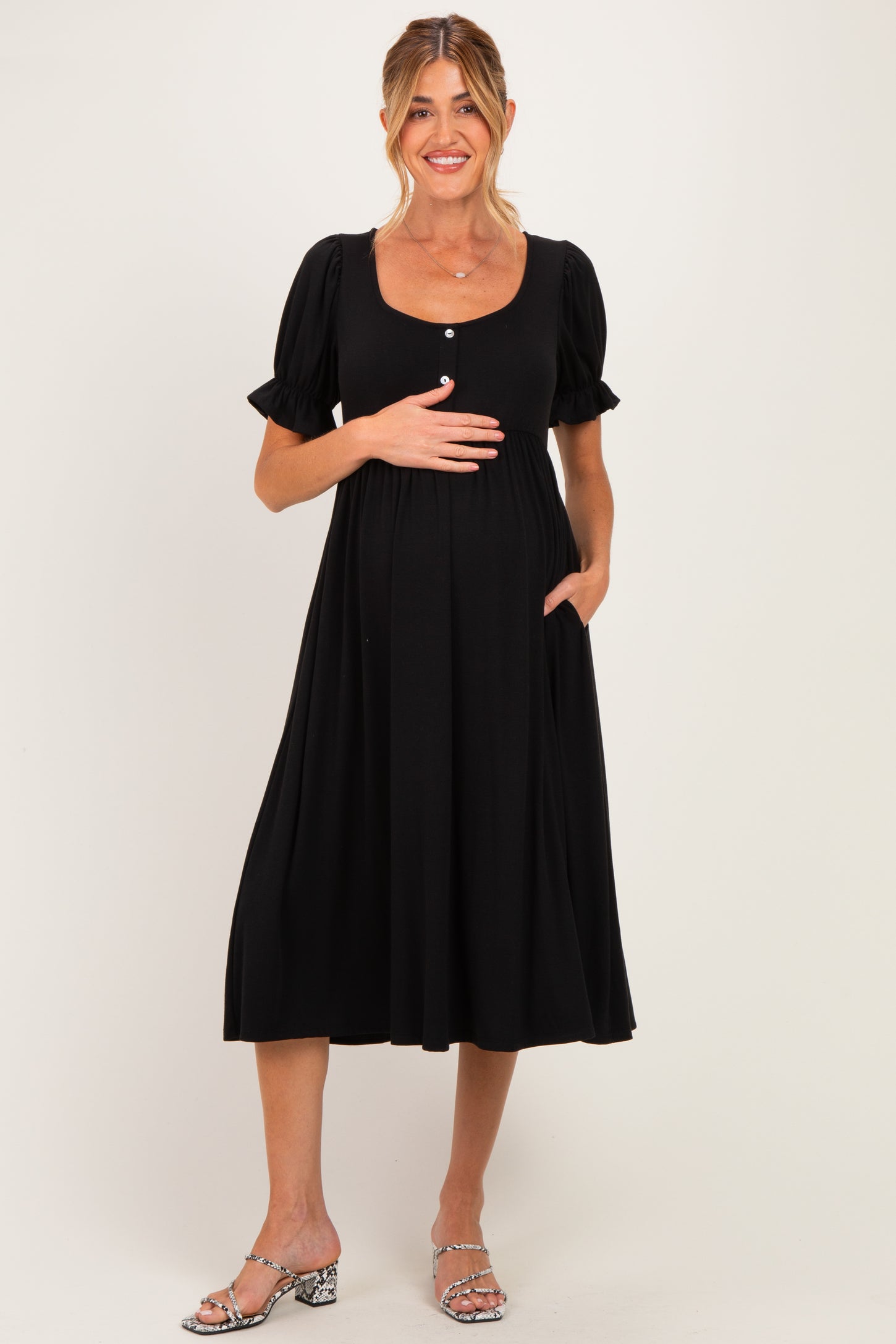 woman wearing a black maternity dress with short puff sleeves and a baby bump, showing side pockets