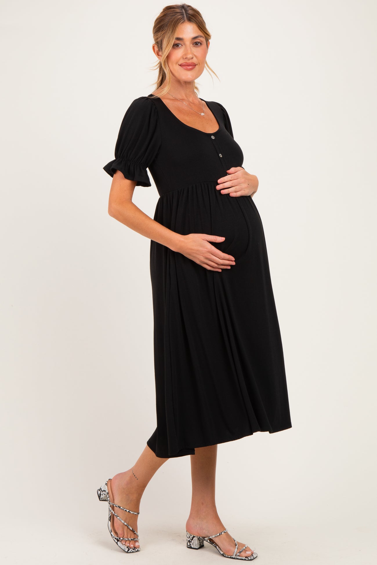 woman wearing a black maternity dress with puff sleeves and buttons, holding her baby bump